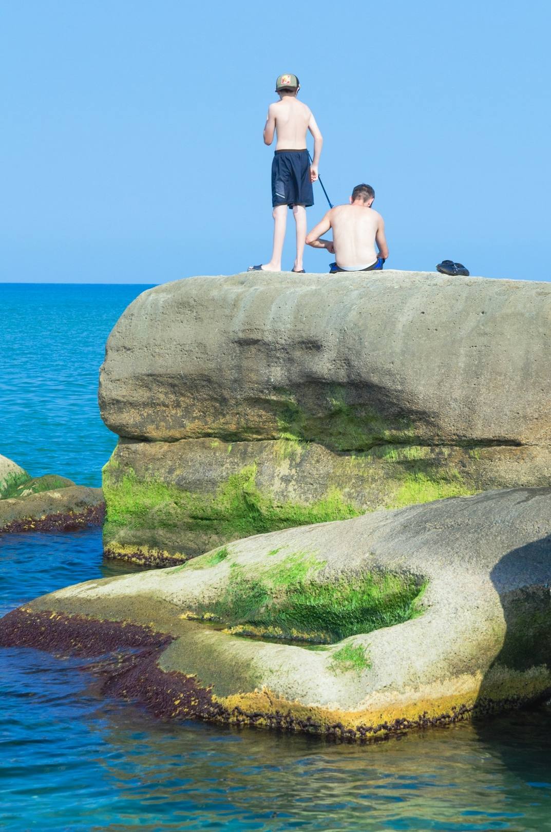 Two people on a mossy rock in a blue sea, unedited
